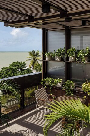 Un balcon avec vue sur l’océan, des plantes en pot et une chaise.