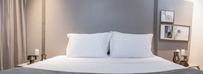 A neatly made bed with white linens and pillows, a bedside table with a lamp, and two framed pictures on the wall. - HCM - Corais De Manaira (João Pessoa)