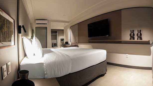 Una habitación de hotel moderna con una cama grande, un televisor de pantalla plana en la pared y una mesita con un florero.