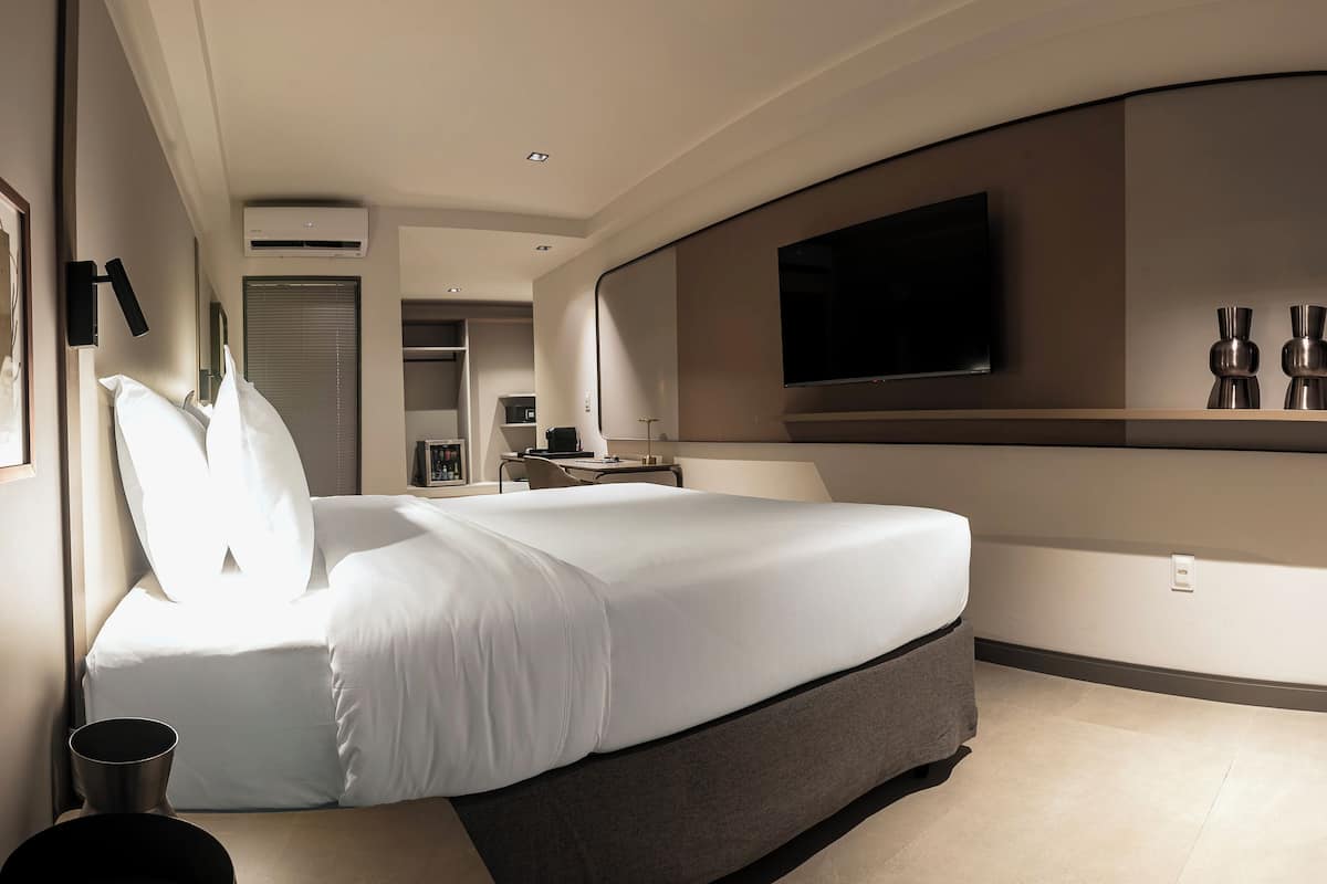 Ein modernes Hotelzimmer mit einem großen Bett, einem flachbildfernseher an der Wand und einem kleinen Tisch mit einer Vase.