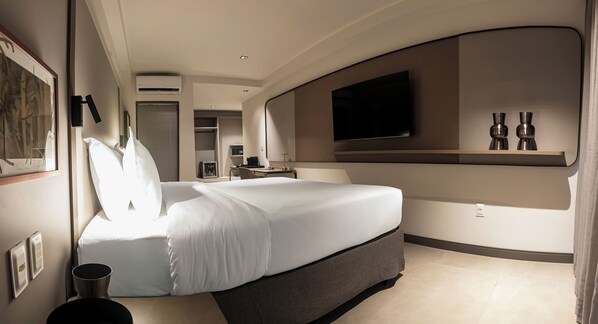 Ein modernes Hotelzimmer mit einem großen Bett, einem flachbildfernseher an der Wand und einem kleinen Tisch mit einer Vase.
