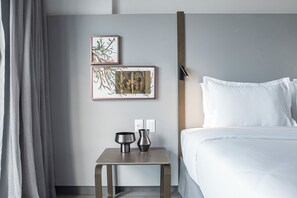 Een hotelkamer met een bed, een nachtkastje met twee decoratieve vazen en twee kunstwerken in lijsten aan de muur.