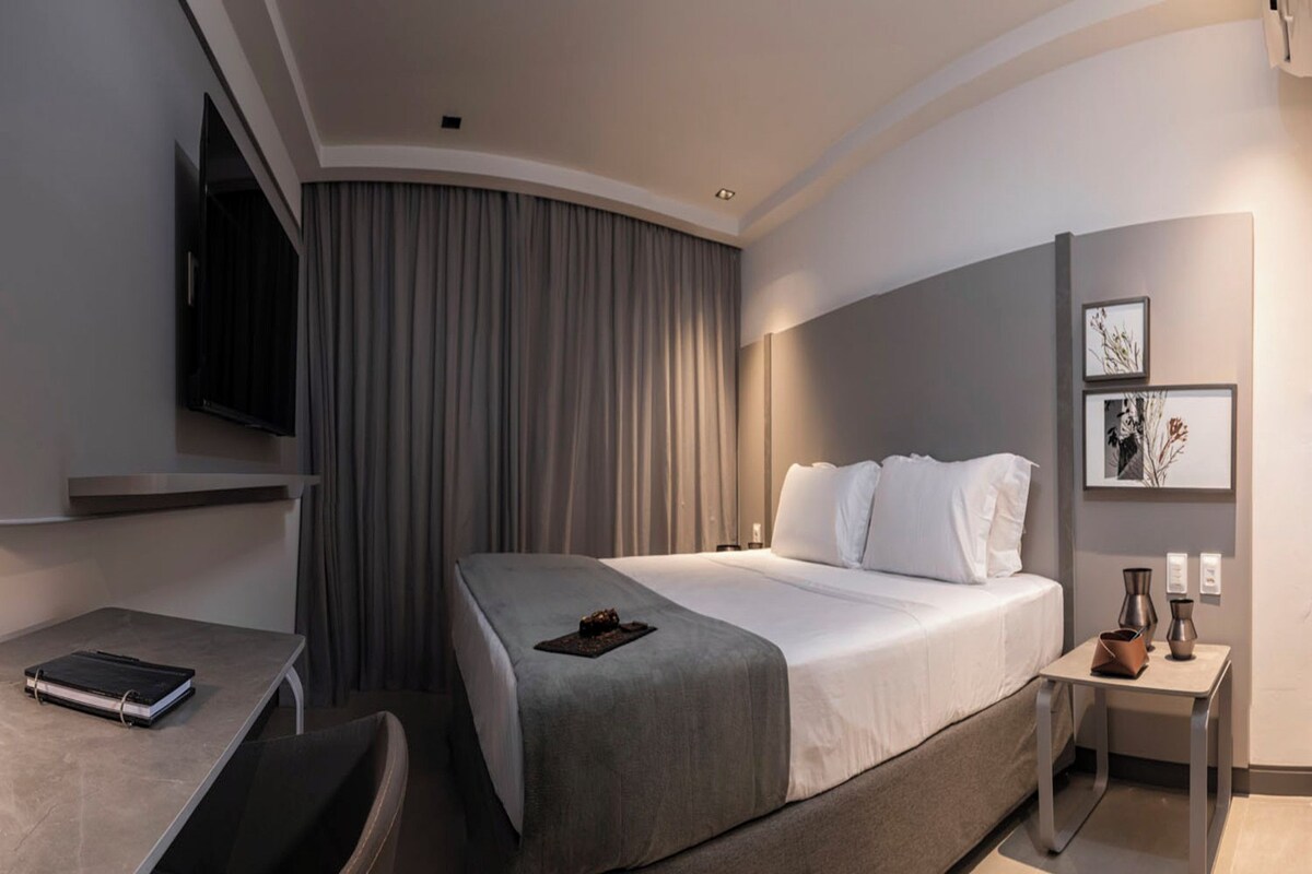 Ein modernes Hotelzimmer mit einem gewölbten Bett, einem Schreibtisch, einem Sessel, einem Flachbildfernseher und einem kleinen Tisch mit Dekoration.