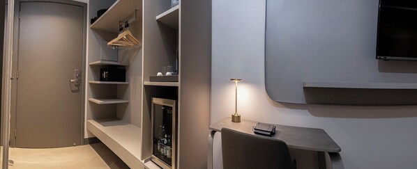 A modern room with a built-in closet, a desk with a lamp, and a flat-screen TV mounted on the wall.