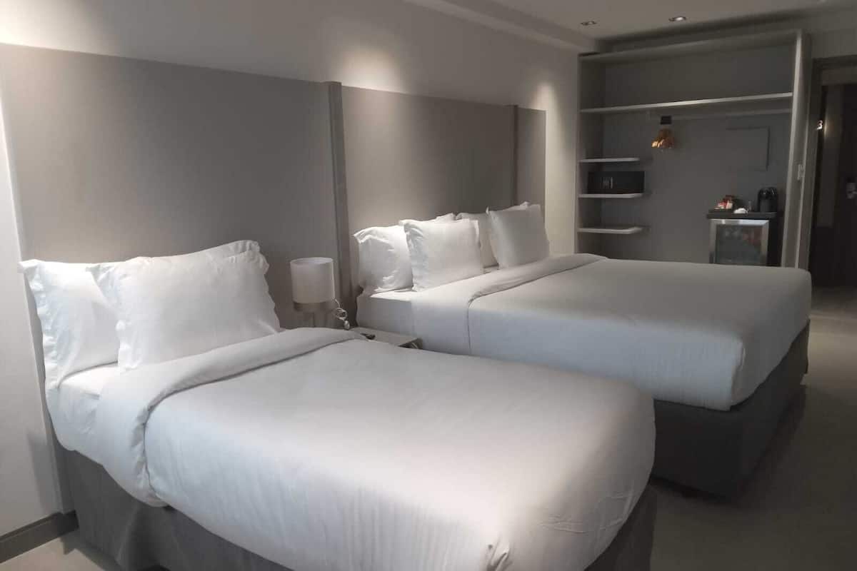 Ein Hotelzimmer mit zwei Betten, einem Nachttisch mit Lampe und einem Schrank mit Regalen.