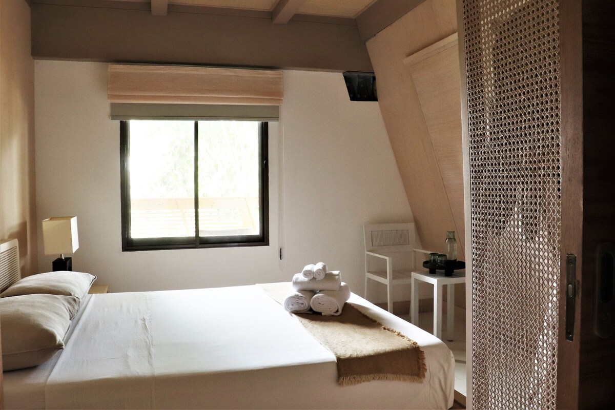 A bedroom with a bed, a window, a nightstand, and a small table with a lamp.
