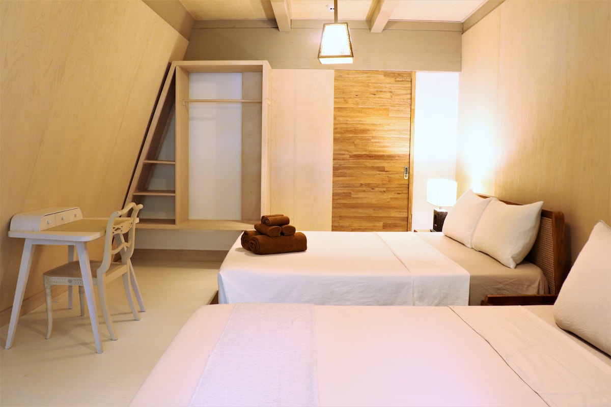 A bedroom with a bed, a desk, and a chair. There is a wooden wall and a ladder leading to a closet.