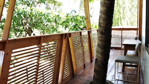 Una terraza de madera con un banco, barandilla de madera y vista a árboles.