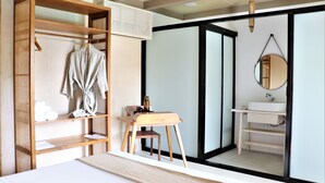 Un dormitorio con un armario de madera, una mesita de noche, un espejo y un baño con lavamanos y estantes.