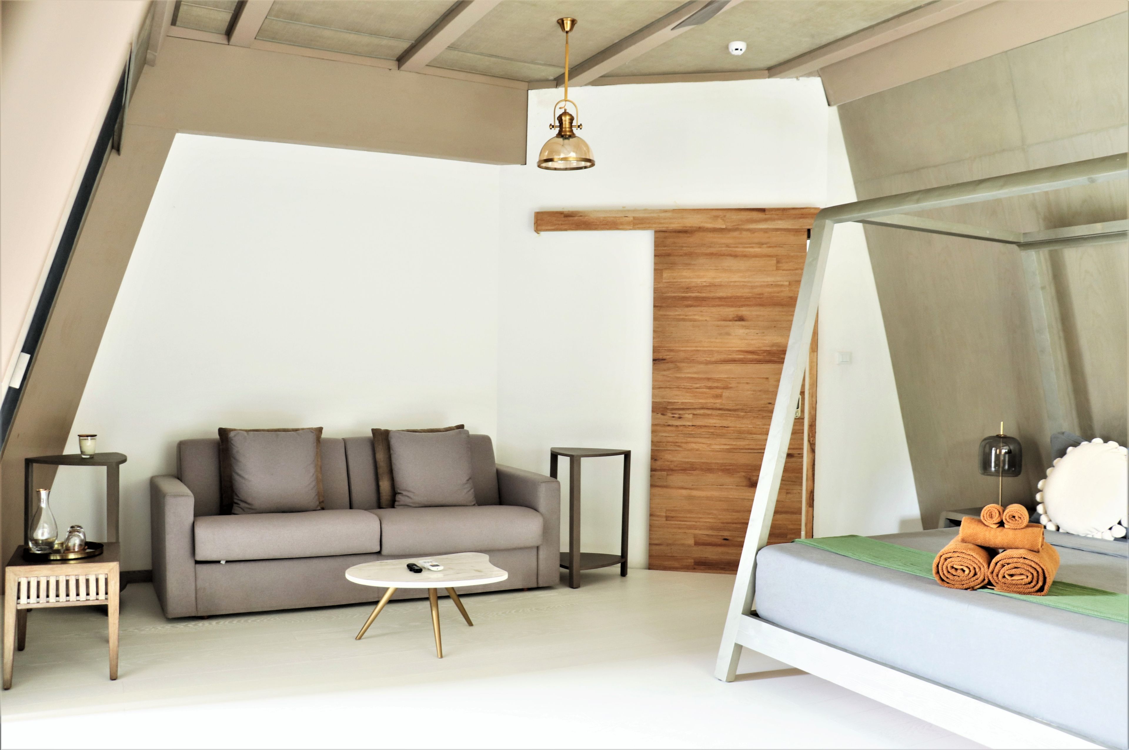 A modern bedroom with a bed, a sofa, a small table, and a hanging light fixture.