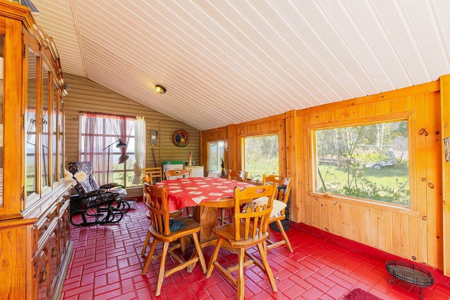 Un chalet confortable doté d’un coin repas avec une nappe rouge, des chaises en bois et une vue sur l’extérieur grâce à de grandes fenêtres.