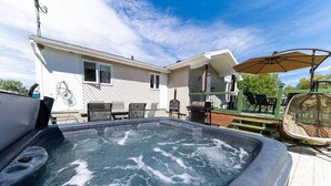 Un jacuzzi con terraza de madera, mobiliario exterior, una parrilla y un patio cubierto.