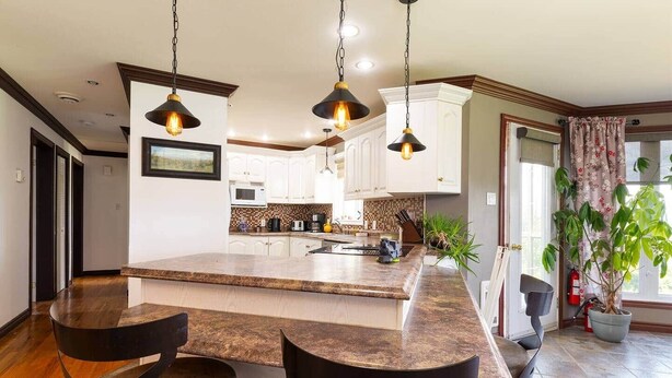 Una cocina amplia con una isla grande, armarios blancos e iluminación colgante.