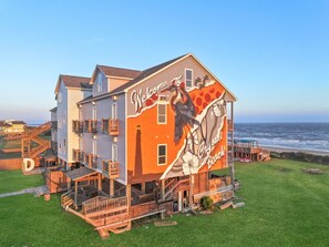 A coastal building with a mural, wooden deck, and ocean view. - Casa Dora - Pool, Games, & Beachfront Fun! (Bolivar Peninsula)