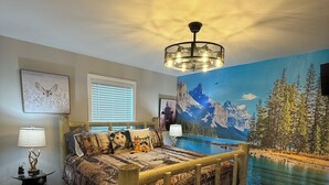 A bedroom with a wooden bed, a mural of a mountain landscape, a chandelier, and a bedside table with a lamp.