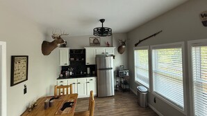 A kitchen with white cabinets, a stainless steel refrigerator, a wooden dining table, and two mounted deer heads.