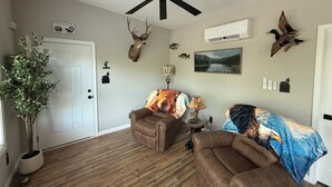 A living room with a ceiling fan, mounted deer head, wall-mounted air conditioner, and a potted plant.
