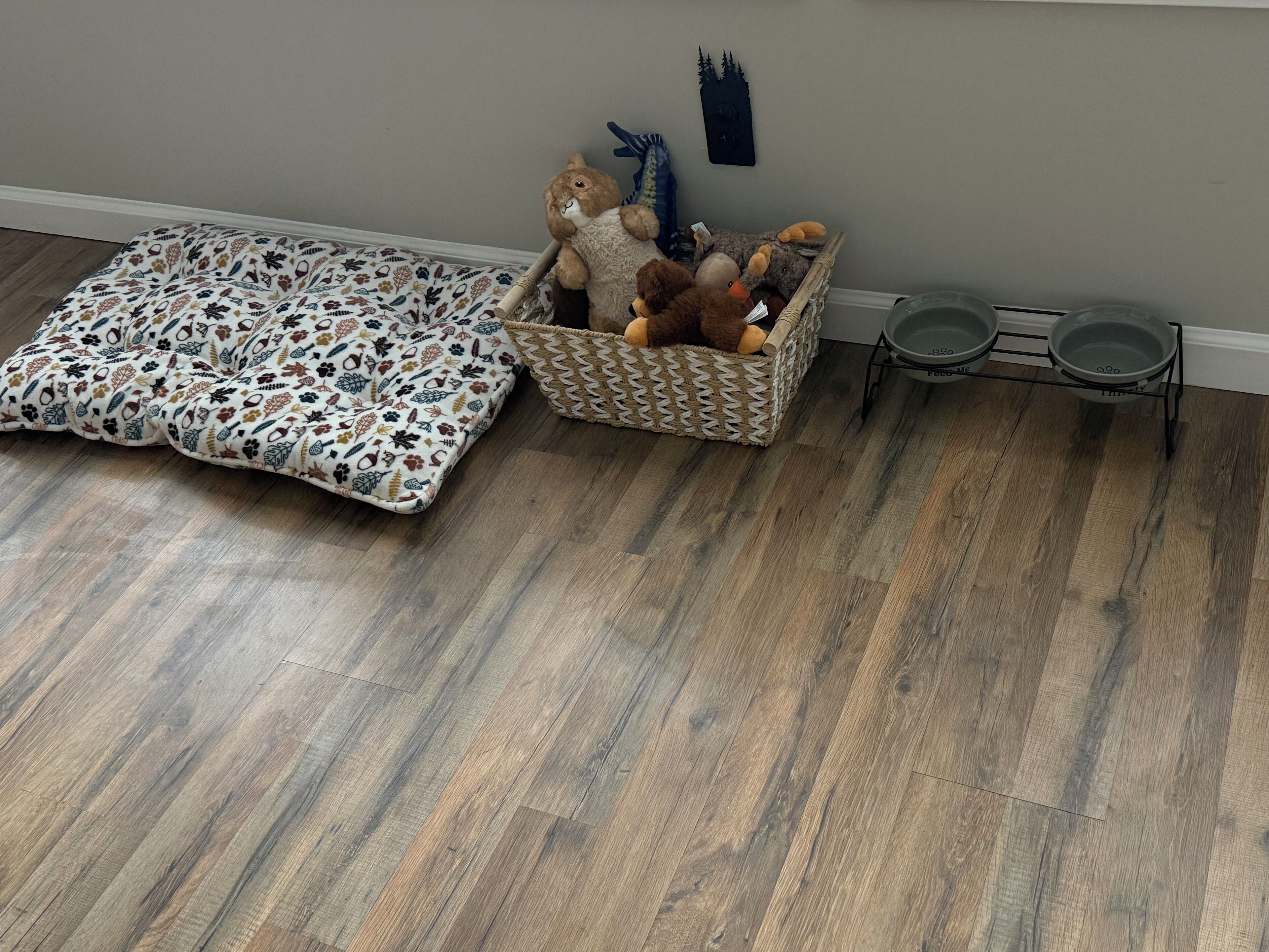 Una habitación con una cama para mascotas estampada, una cesta de mimbre con peluches y un comedero para mascotas.