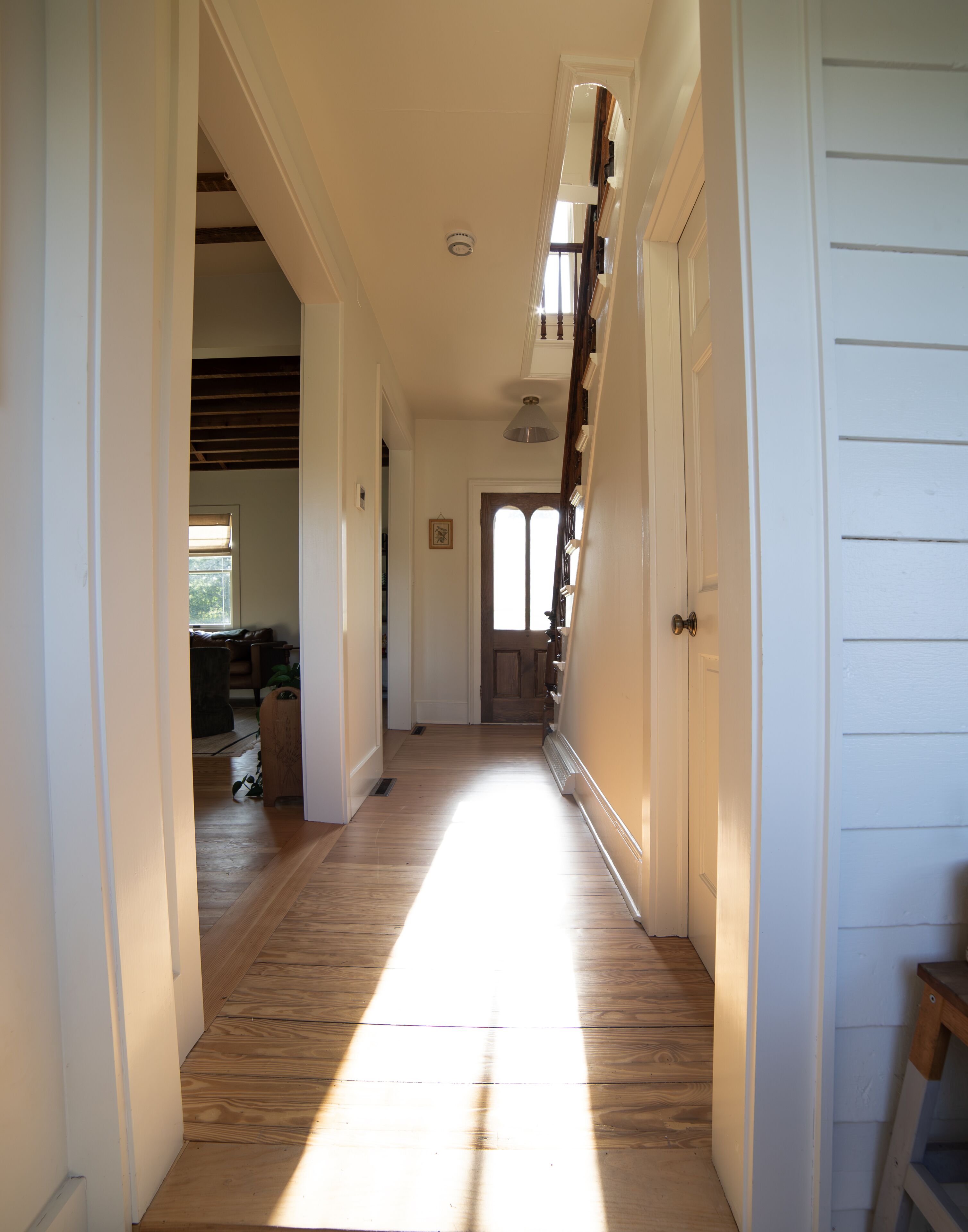 Un couloir doté d’un plancher en bois, de murs blancs et d’une porte au fond.
