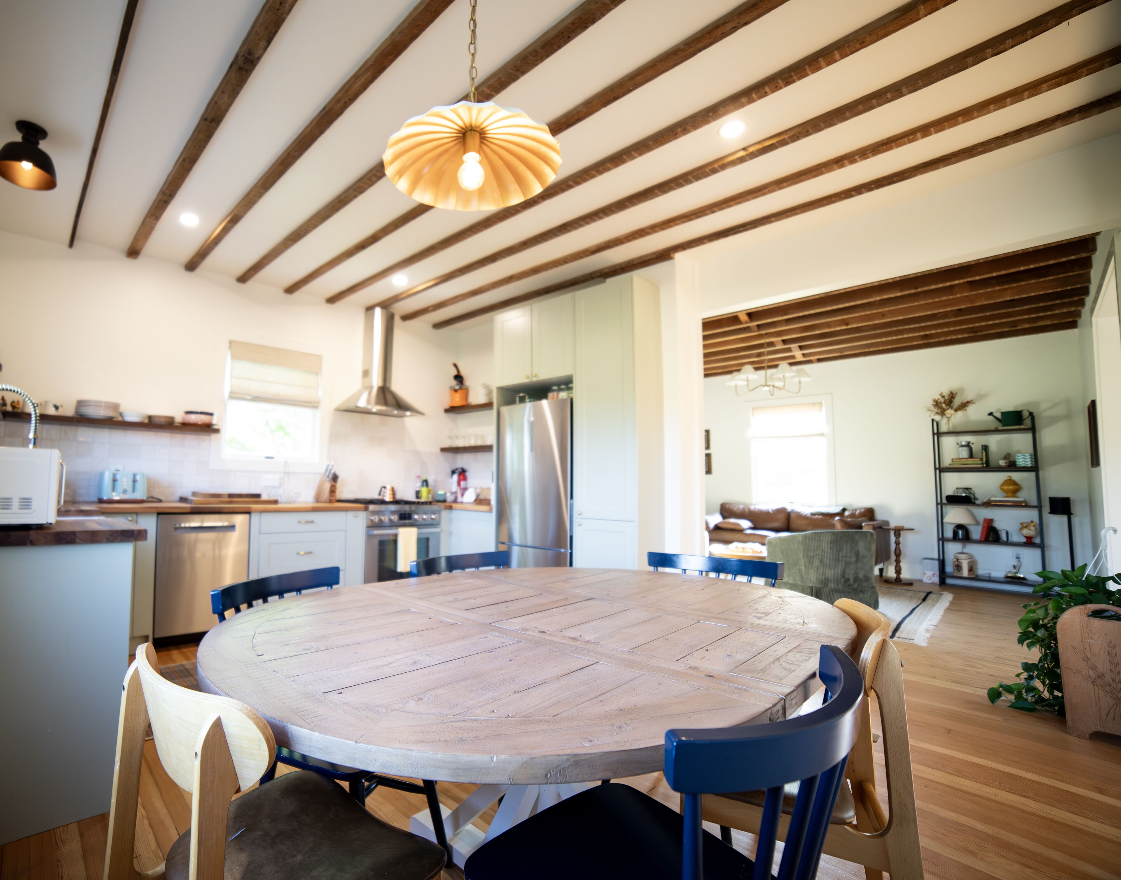 Une cuisine moderne dotée d’un îlot central, de poutres en bois au plafond et d’une table de salle à manger ronde, accompagnée de chaises.