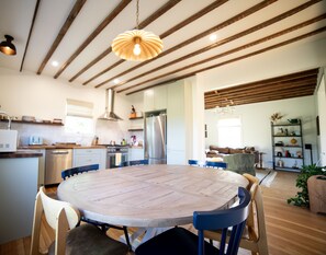 A modern kitchen with a central island, wooden ceiling beams, and a round dining table with chairs.