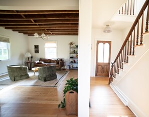 A spacious living room with a high ceiling, a wooden staircase, and a door with a window.