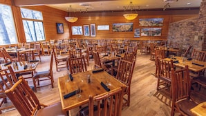Un restaurant spacieux avec des tables et des chaises en bois, de grandes fenêtres et des œuvres d’art accrochées aux murs.