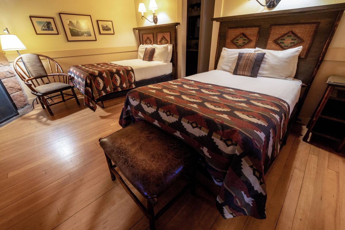 Habitación de hotel con dos camas, un banco de madera, una silla y cuadros en la pared.