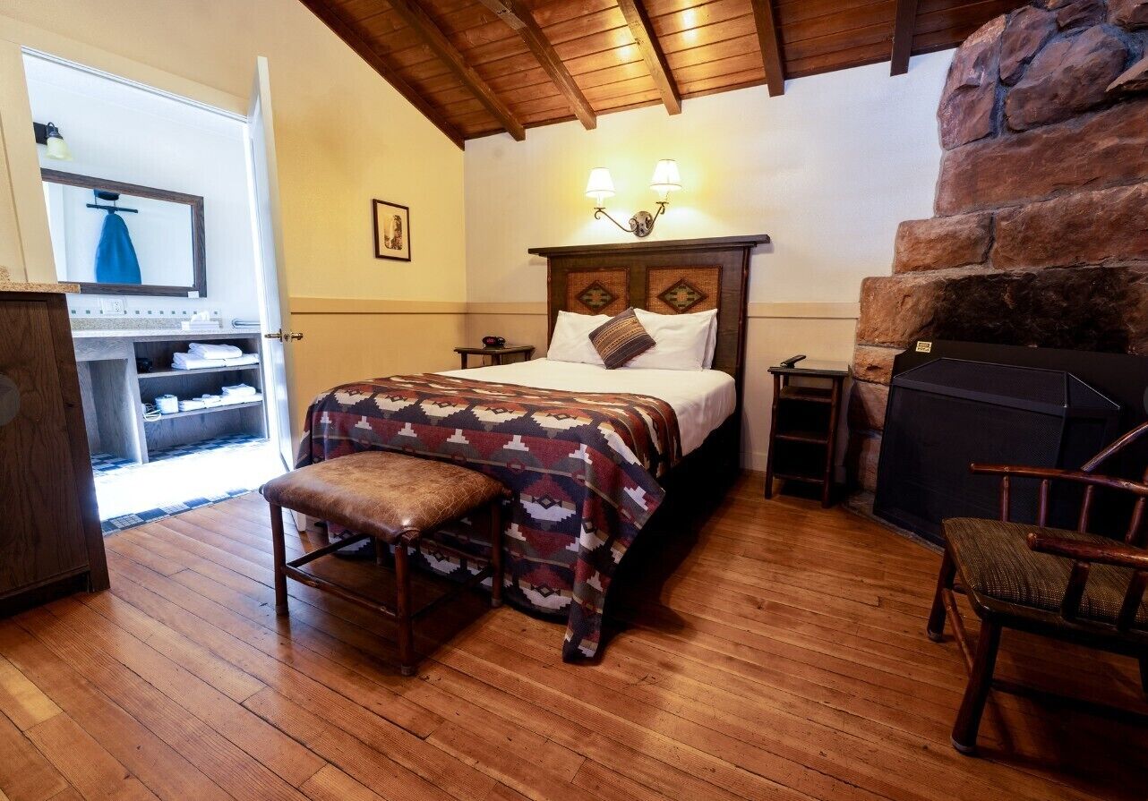 Un dormitorio con cama, banca, mesita de noche y chimenea.