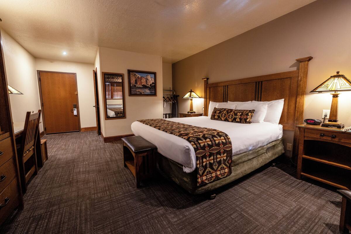 Una habitación de hotel con una cama grande, mesitas de noche, un escritorio y una silla.