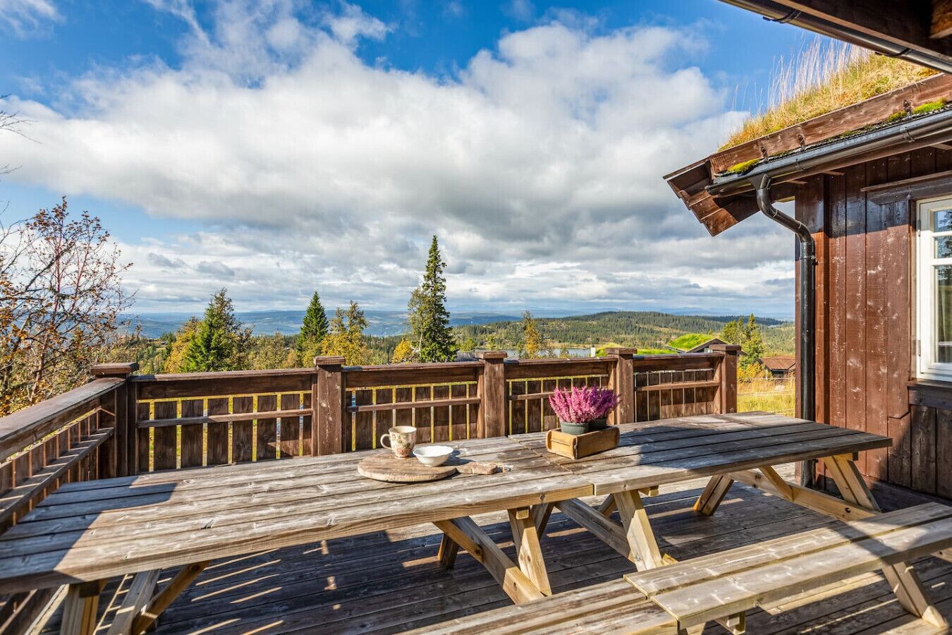 En träveranda med ett bord och stolar, med utsikt över ett vackert landskap med träd och berg.