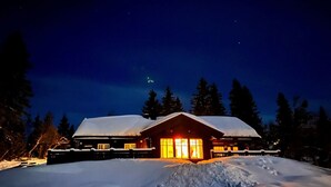 A lodge with a snow-covered roof, large windows, and a well-lit entrance.