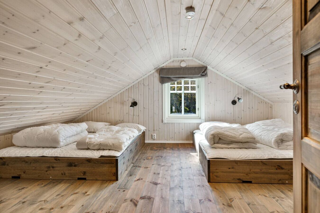 A cozy attic bedroom with two beds, wooden floors, and a sloped ceiling.