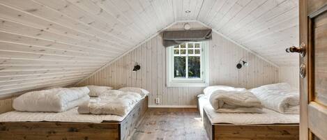 A cozy attic bedroom with two beds, wooden floors, and a sloped ceiling.