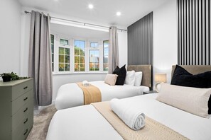 A modern hotel room with two beds, a bedside table, a lamp, and a view of the outside.