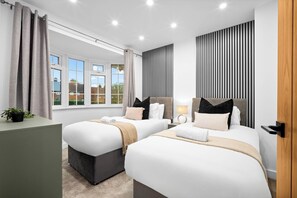 A modern hotel room with two beds, a desk, and a window with curtains.
