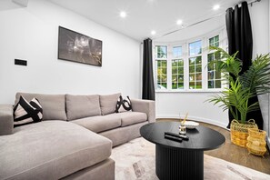 Ein modernes Wohnzimmer mit einer Eckcouch, einem runden Couchtisch und einem großen Fenster mit Vorhängen.