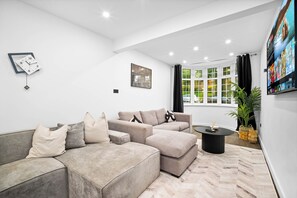 Ein modernes Wohnzimmer mit einem Ecksofa, einem Couchtisch und einem großen Fenster mit Vorhängen.