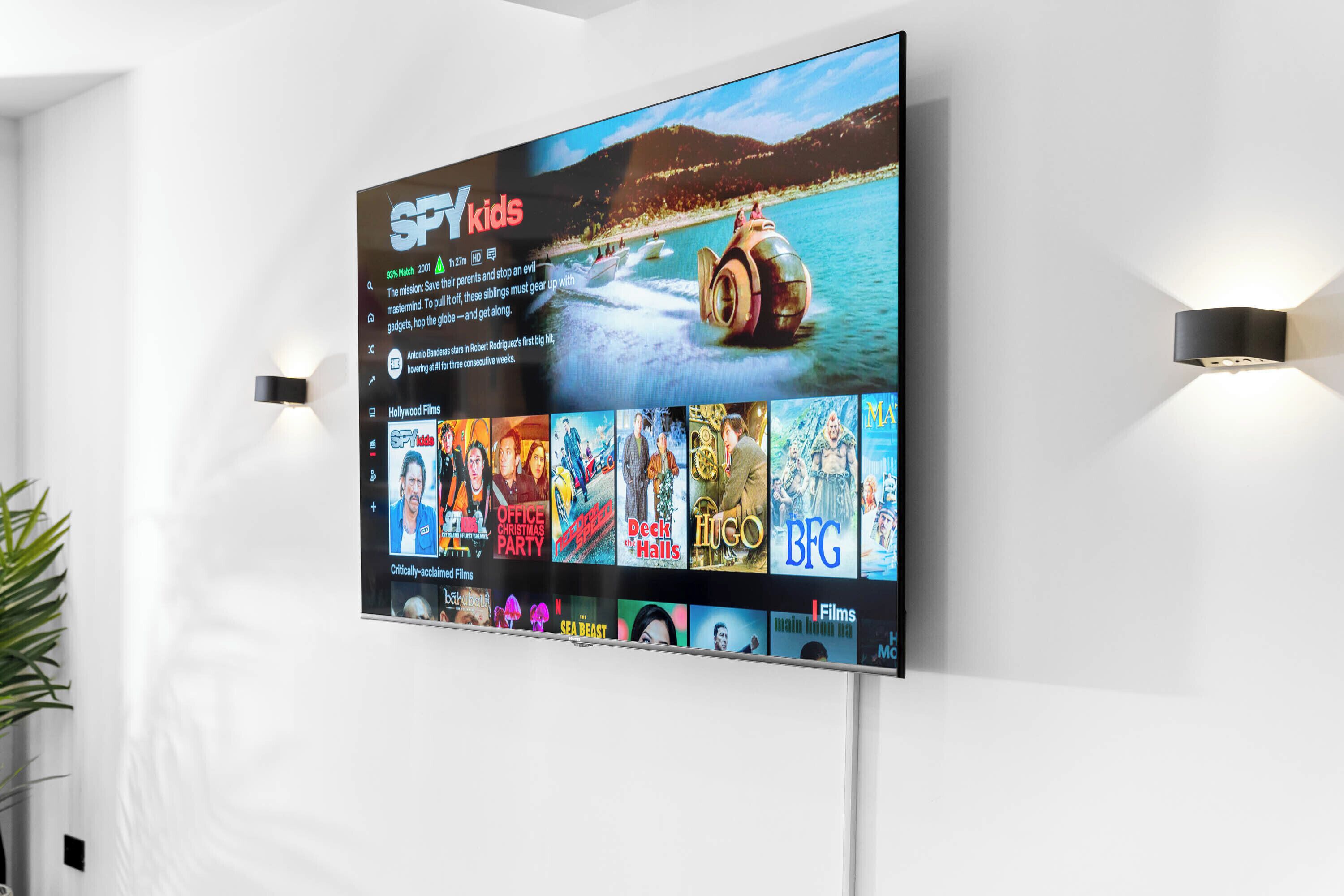 A flat-screen TV mounted on a white wall displaying a movie selection interface with various film options.