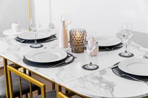 A dining table set with plates, cutlery, and glasses, with a marble top and gold chair legs.