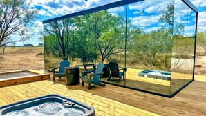 Una terrazza esterna moderna con struttura in vetro, pavimento in legno e vasca idromassaggio.