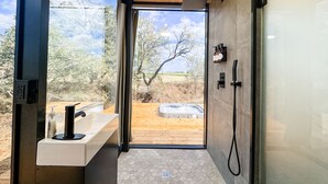 Un bagno moderno con soffitto in legno, box doccia in vetro, un piccolo terrazzo esterno in legno e vista su un paesaggio desertico.