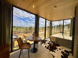 Una habitación moderna con ventanas amplias, una mesa redonda, una cama y un tapete de cuero de vaca.