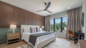 Une chambre moderne avec un grand lit, un ventilateur de plafond, une table de chevet, un bureau et une vue sur l’extérieur.