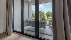 Une chambre moderne dotée d’une porte-fenêtre coulissante donnant sur un balcon extérieur avec une table et des chaises.
