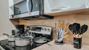 A kitchen with a stove, microwave, kettle, pots, and a utensil holder. - Walnut Premium / King Bed / 65" TV / Ping-Pong (Philadelphia)