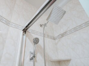 A corner of a bathroom with white tiles, a showerhead, and a handheld shower attachment.