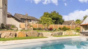 Ein Swimmingpool mit Holzterrasse, einer Steinmauer und einem Baum im Hintergrund.