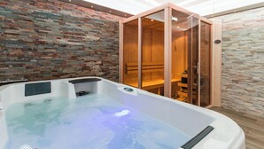 Un espace bien-être comprenant un bain à remous, des bancs en bois et un sauna à parois vitrées.