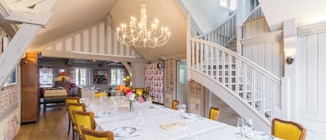 A dining area with a long table set for a meal, a chandelier, and a staircase leading to an upper level.